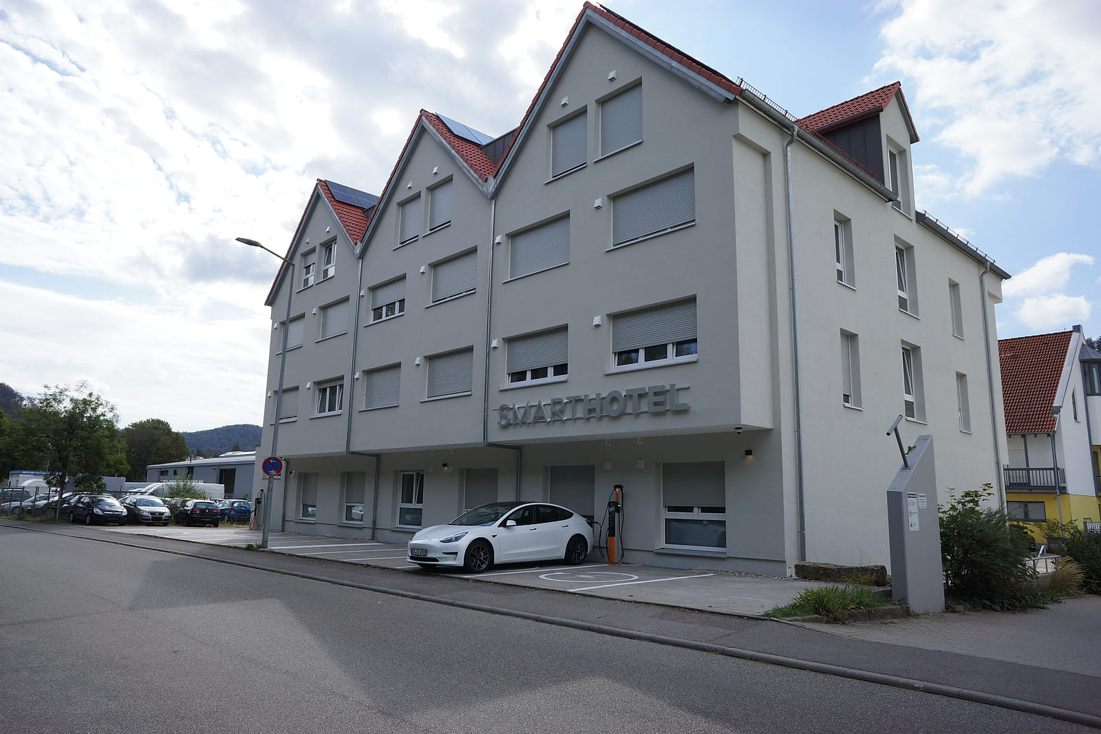 Das Hotel in Aalen-Unterkochen an der Straße, davor Stellplätze und ein ladendes Elektroauto.