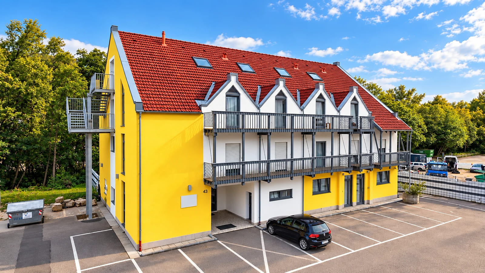 Das zweite Gebäude in der Kochertalstraße 43: gelb-weiße Fassade mit umlaufenden Balkonen und eigenen Stellplätzen davor.
