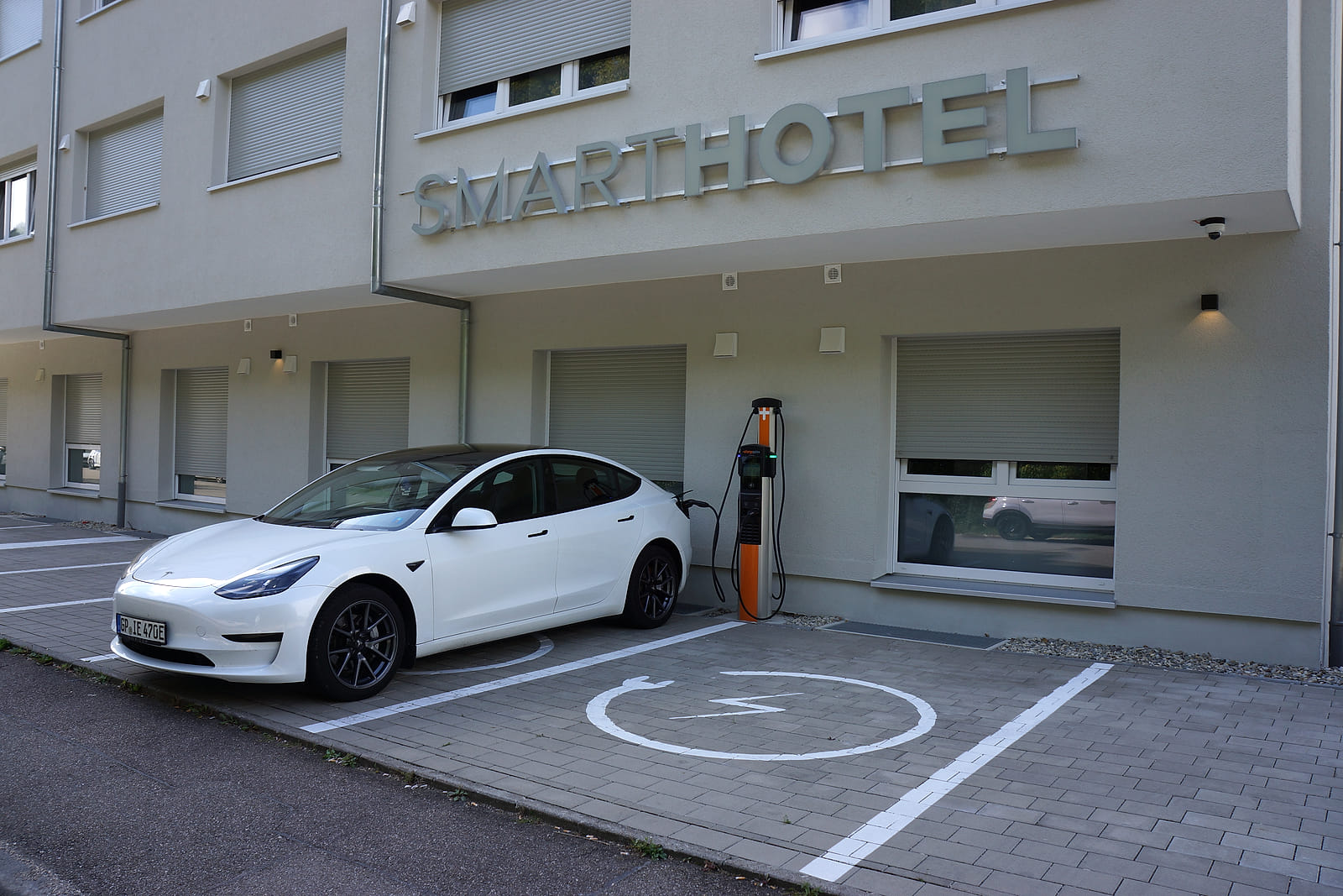 Elektroauto lädt an der Ladesäule vor dem Gebäude mit dem Schriftzug SMARTHOTEL.
