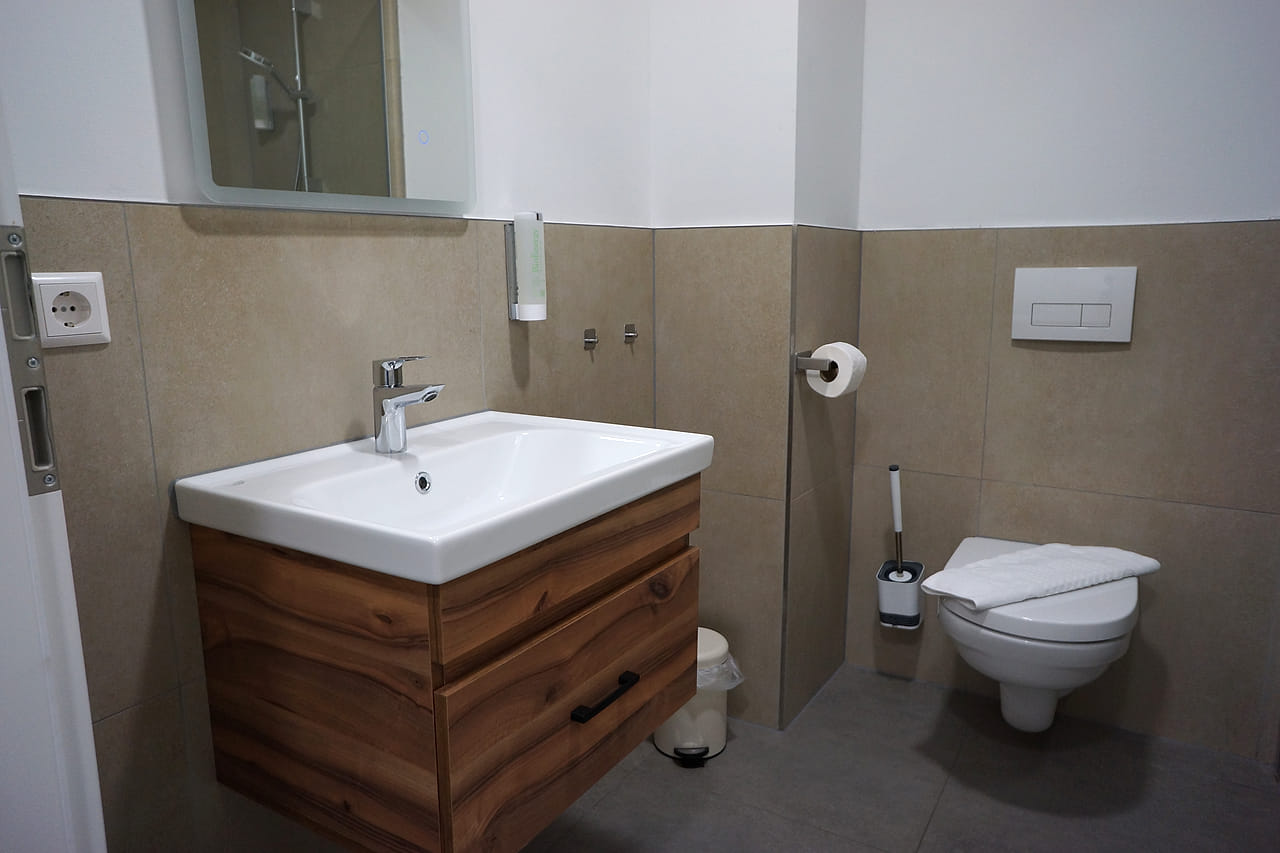 Bad mit breitem Waschtisch, Spiegel, Wand-WC und Dusche.