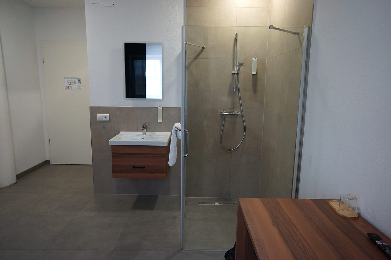Bodengleiche Dusche hinter Glas, Waschtisch mit beleuchtetem Spiegel.