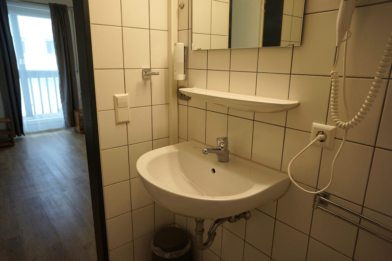 Gefliestes Bad mit Waschbecken, Spiegel und Föhn an der Wand.