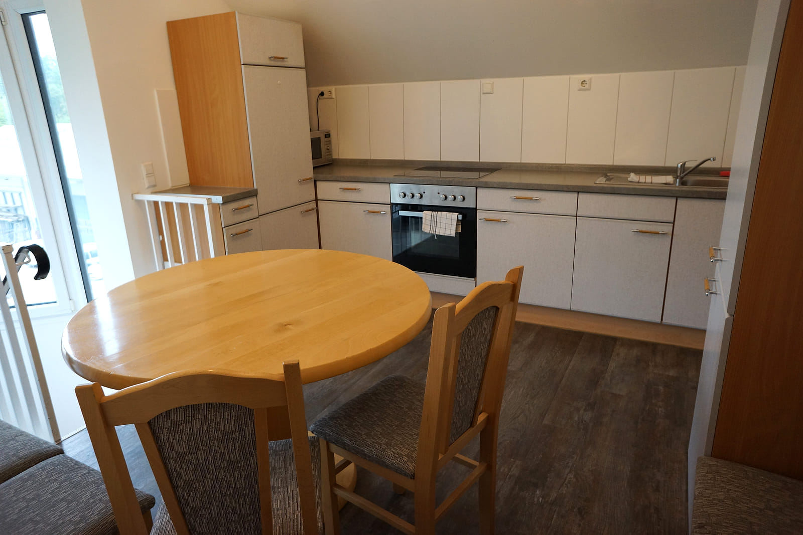 Küche des WG Apartments mit Backofen, Spüle, Hängeschränken und rundem Esstisch mit Stühlen.