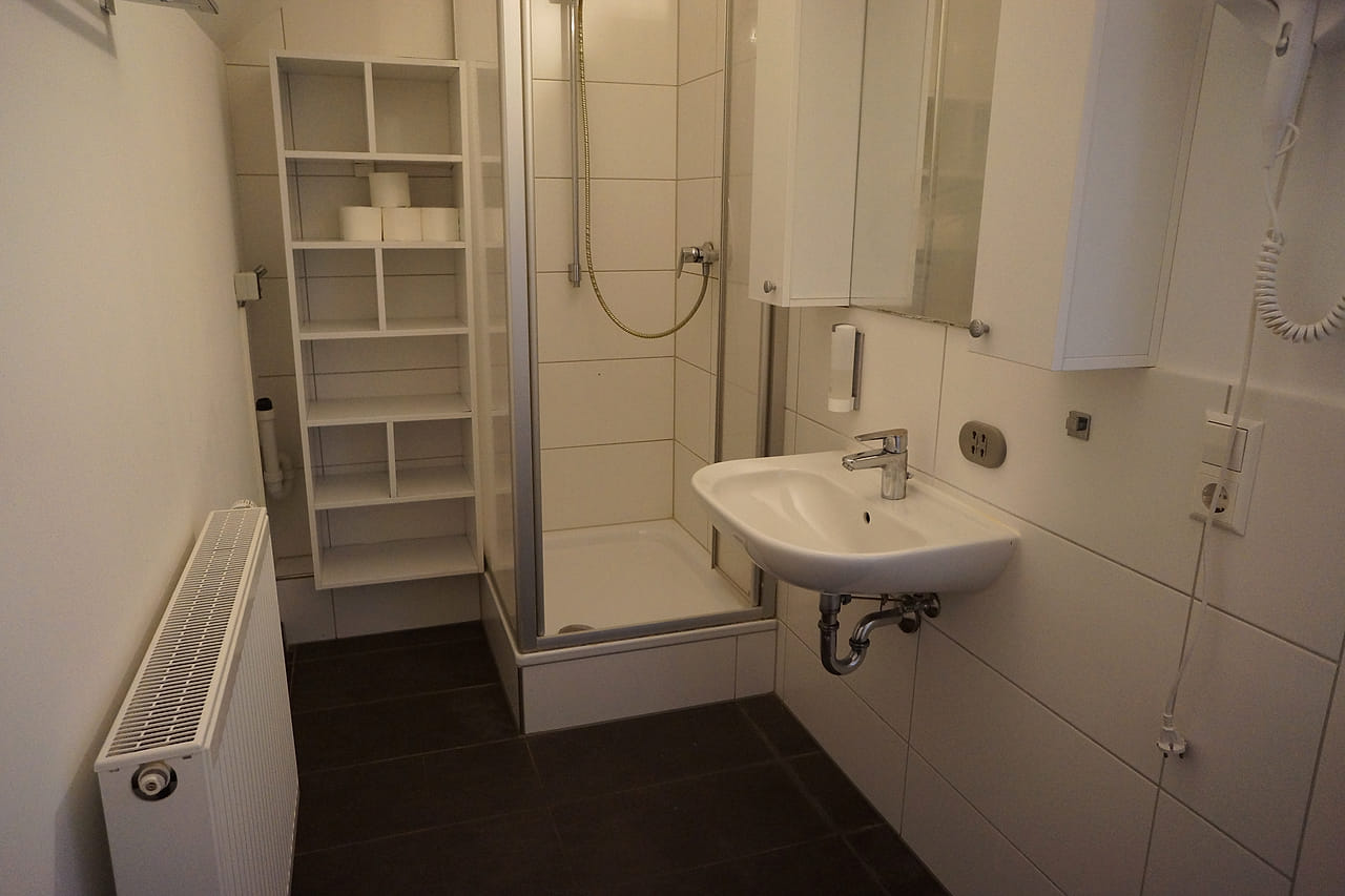 Bad im WG Apartment mit Duschkabine, Waschbecken und Regal.